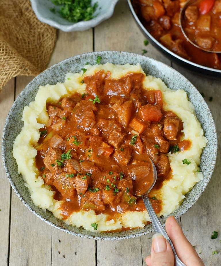Hungarian vegan goulash in a bowl over mashed potatoes