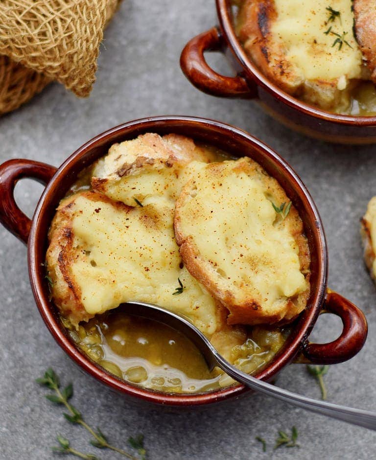 Vegane französische Zwiebelsuppe mit Linsen und Käsebaguette in einer braunen Schüssel