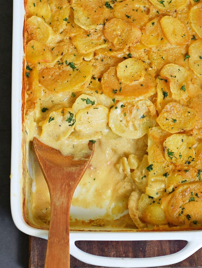 vegan scalloped potatoes with wooden spoon in a white baking dish