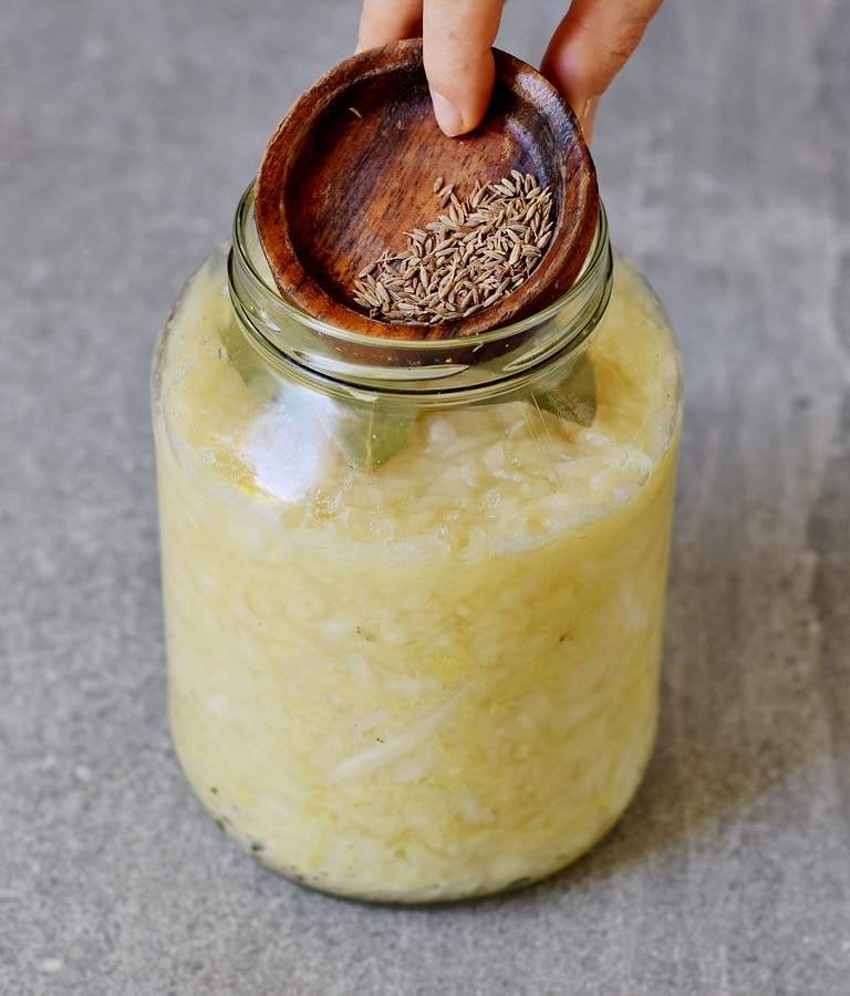 Adding caraway seeds to a jar of sauerkraut