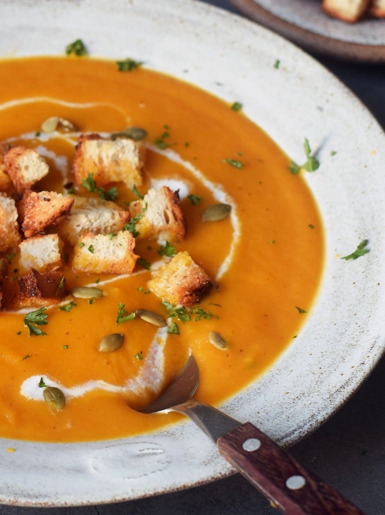 Nahaufnahme einer Karottensuppe in einer grauen Schüssel mit Croutons
