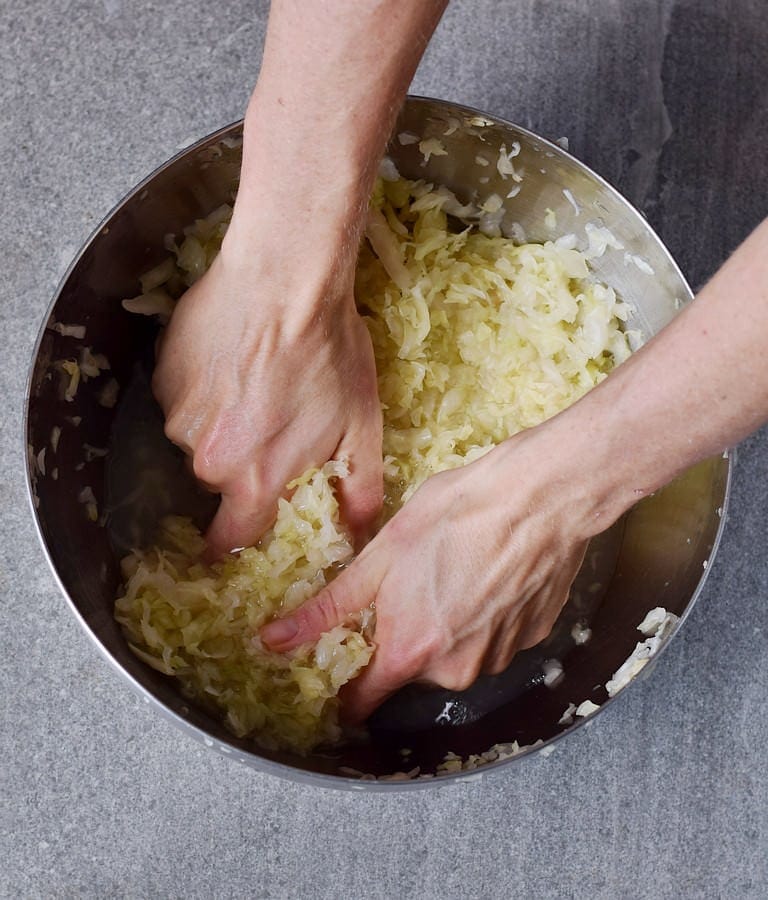 Hands kneading cabbage in a large silver bowl