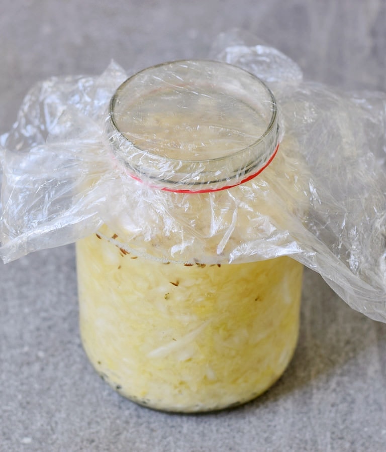Jar filled with sauerkraut covered with plastic wrap