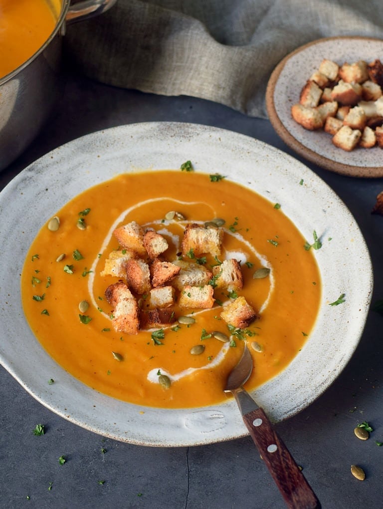 Vegan carrot and ginger soup in a gray bowl with croutons