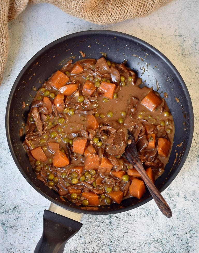 Pilzragout (vegan) mit Erbsen und Karotten in einer schwarzen Pfanne