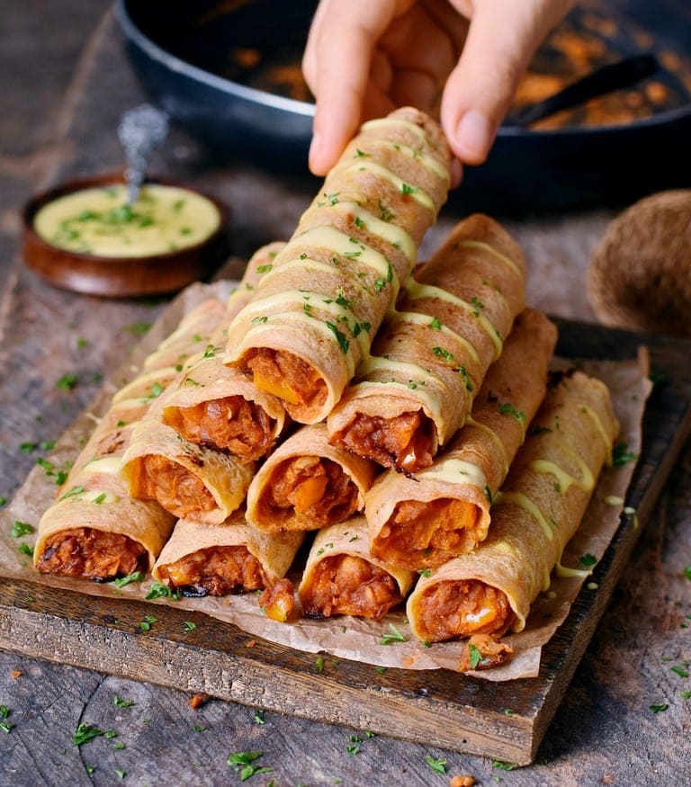 Hand grabbing Baked Buffalo chickpea taquitos with vegan cheese drizzle