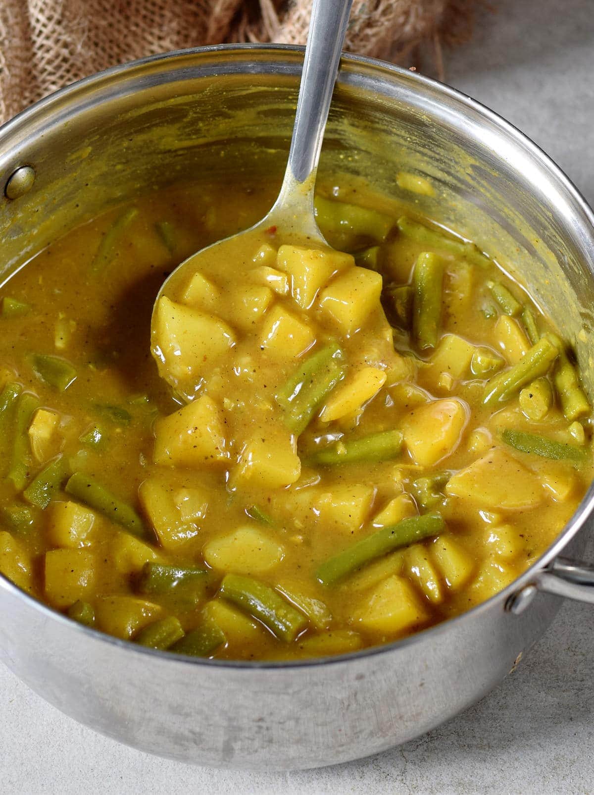 Veganes Kartoffel Curry mit grünen Bohnen in einem Topf mit Schöpfkelle
