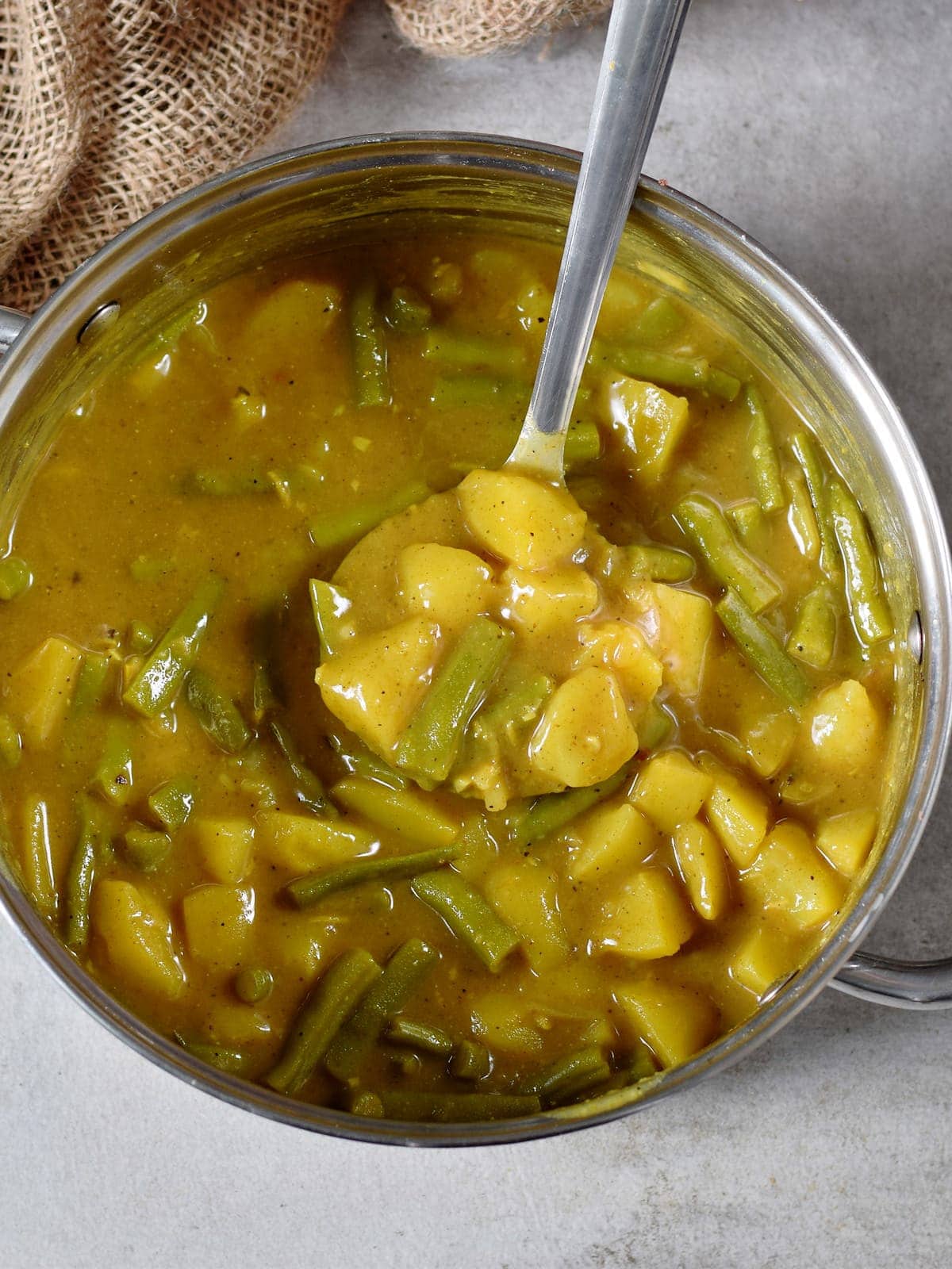 Veganes Curry mit Kartoffeln und grünen Bohnen in einem großen Topf mit Schöpfkelle von oben