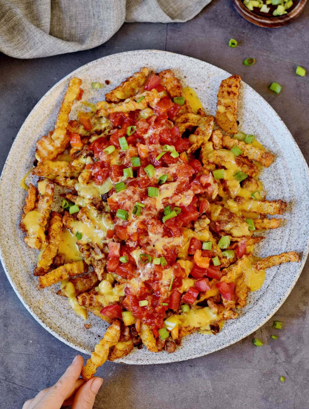 hand grabbing nacho fries loaded with salsa and vegan cheese