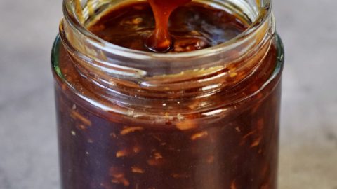 spoon drizzling chinese garlic sauce into glass jar
