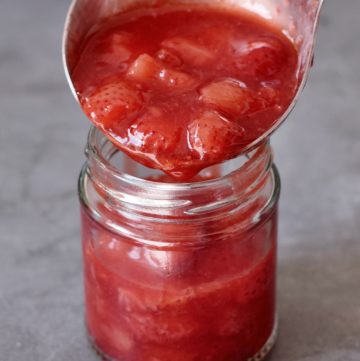A ladle filled with strawberry compote over a glass jar