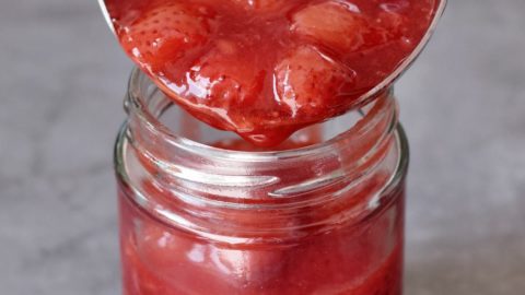 A ladle filled with strawberry compote over a glass jar
