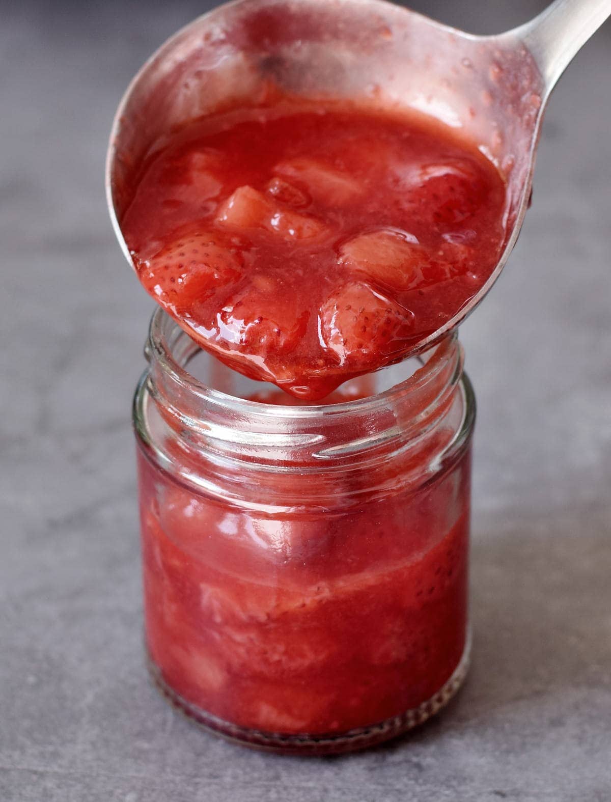Ladle fills strawberry compote into a glass jar