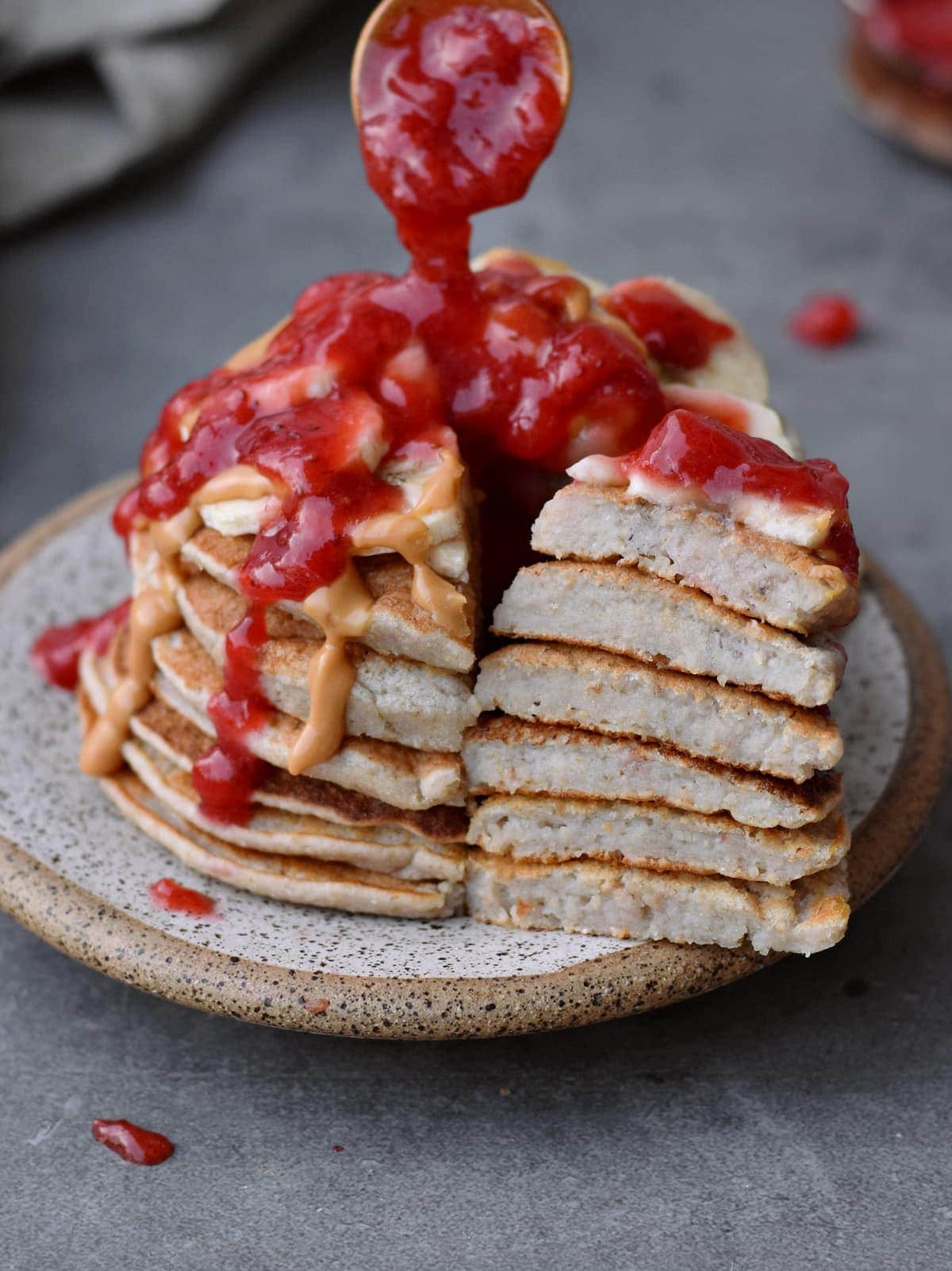 Ein Turm Pfannkuchen mit Erdnussmus und Erdbeersoße auf einem kleinen Teller