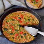 Veggie frittata in a cast iron skillet with a piece on a small plate