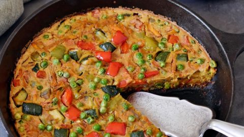 Veggie frittata in a cast iron skillet with a piece on a small plate