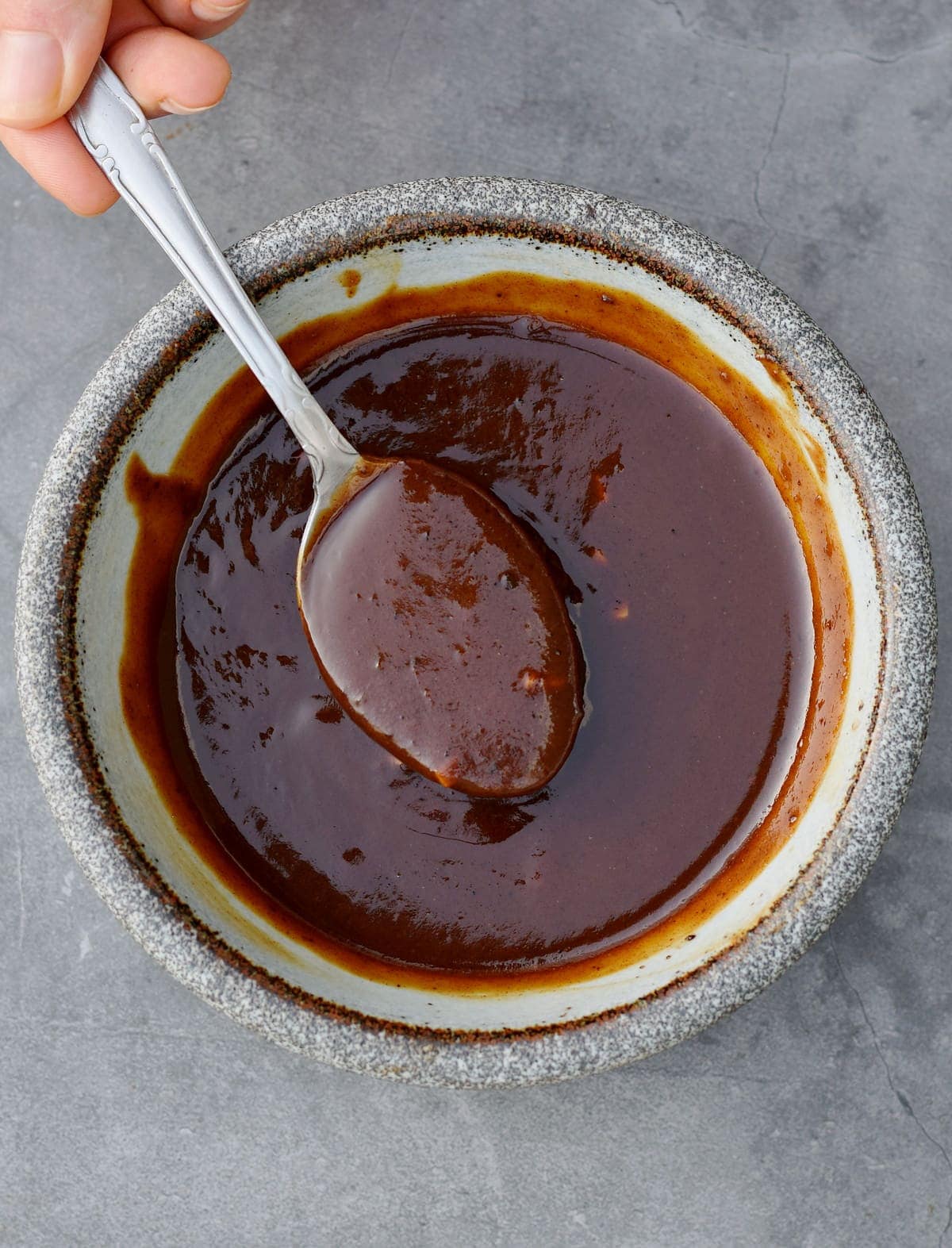 hand holding spoon submerged in homemade hoisin sauce