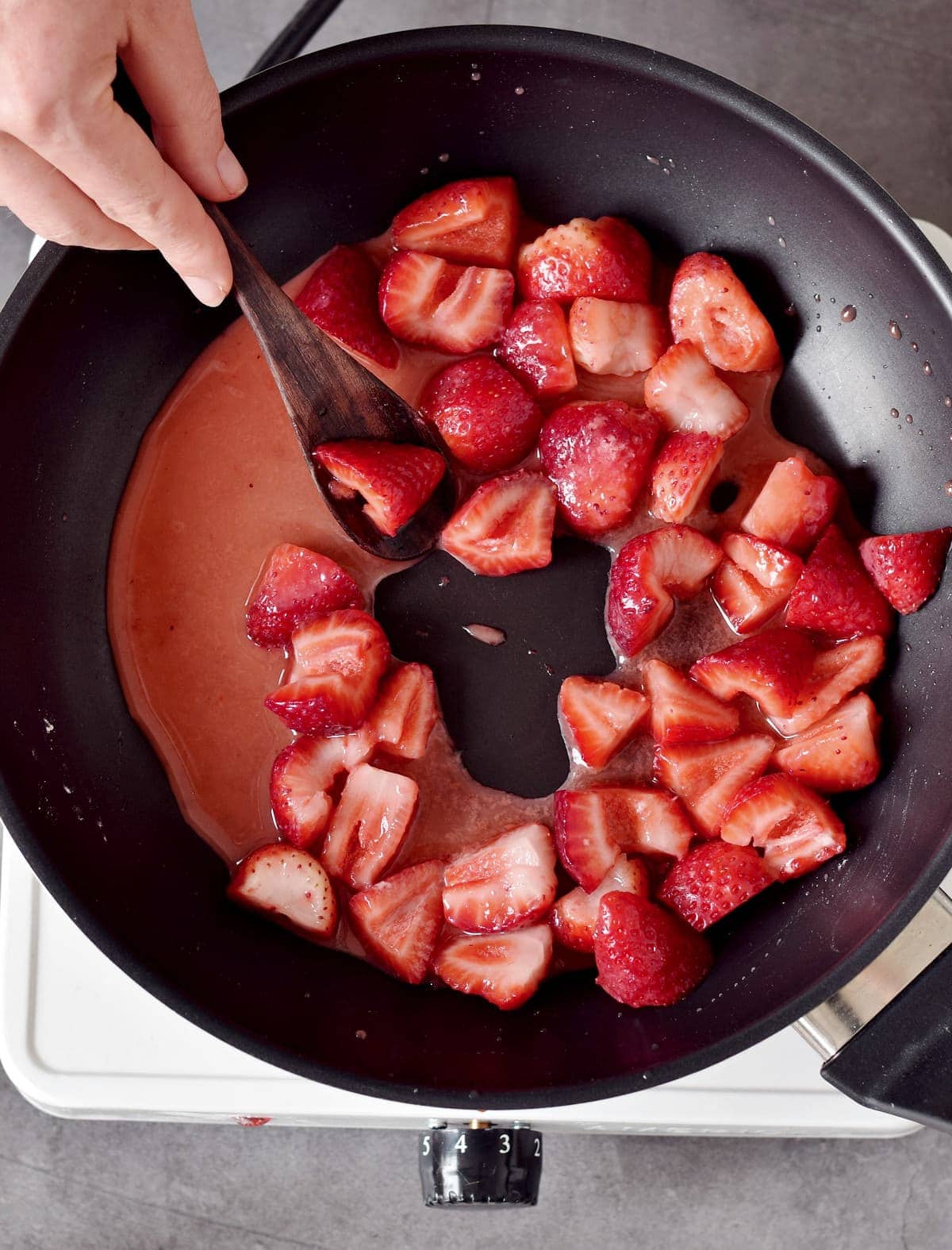 stirring small pieces of strawberries in a black pan
