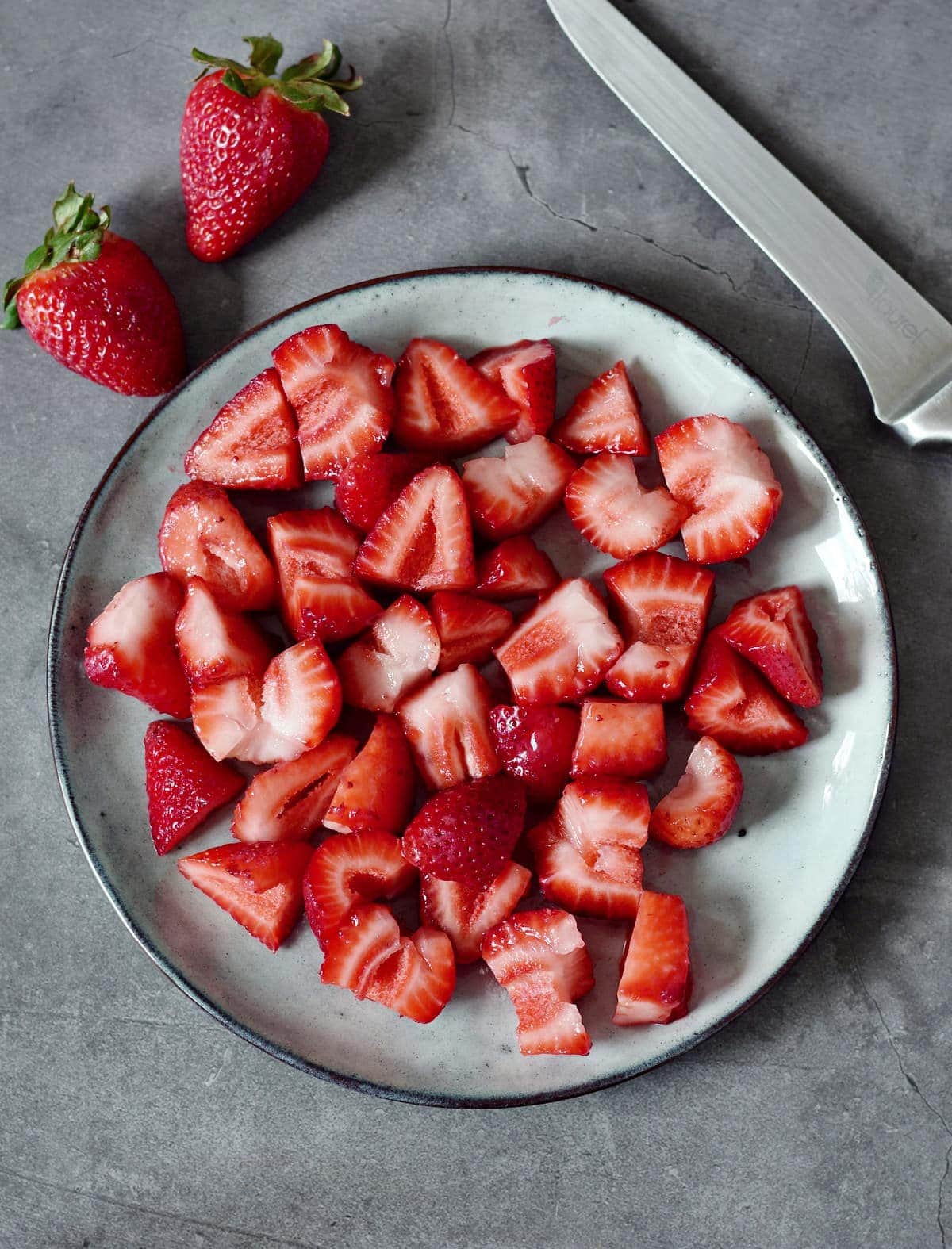 Frische Erdbeeren in Stücke geschnitten auf einem grauen Teller