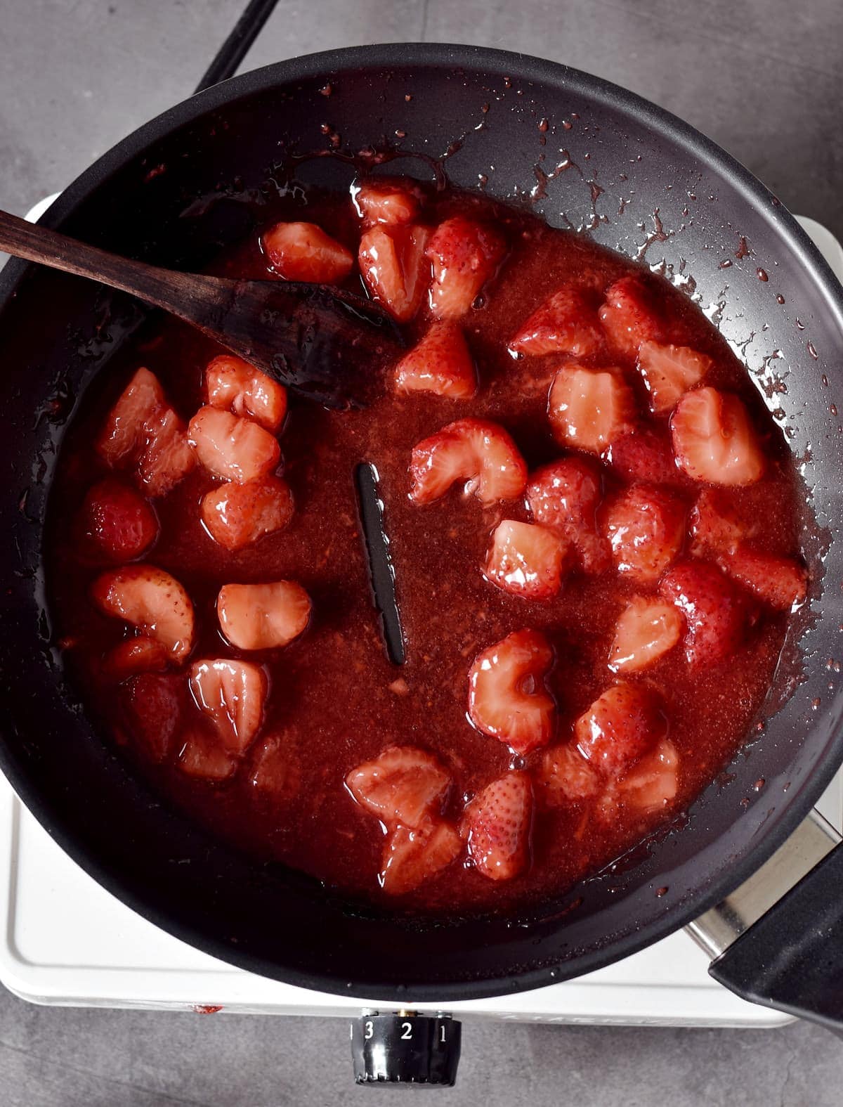 Eingedicktes Erdbeer Kompott mit Holzöffel in einer schwarzen Pfanne