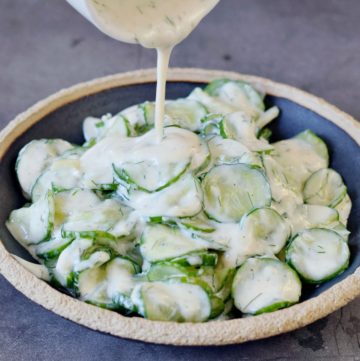 Pouring creamy dill dressing over German cucumber salad