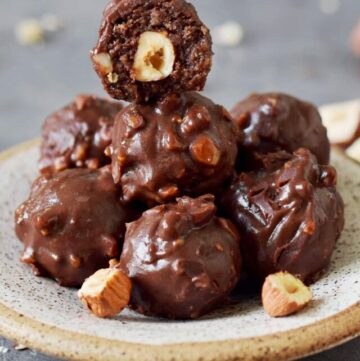 7 homemade Ferrero Rocher truffles on a small plate with one showing the inside