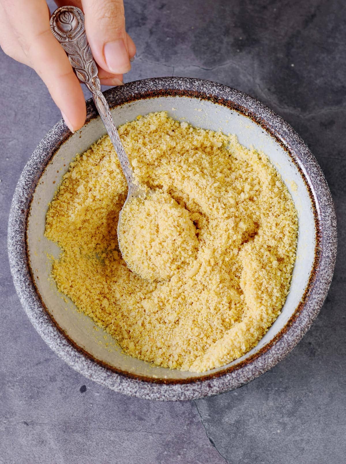 hand holding a spoon submerged in vegan parmesan cheese