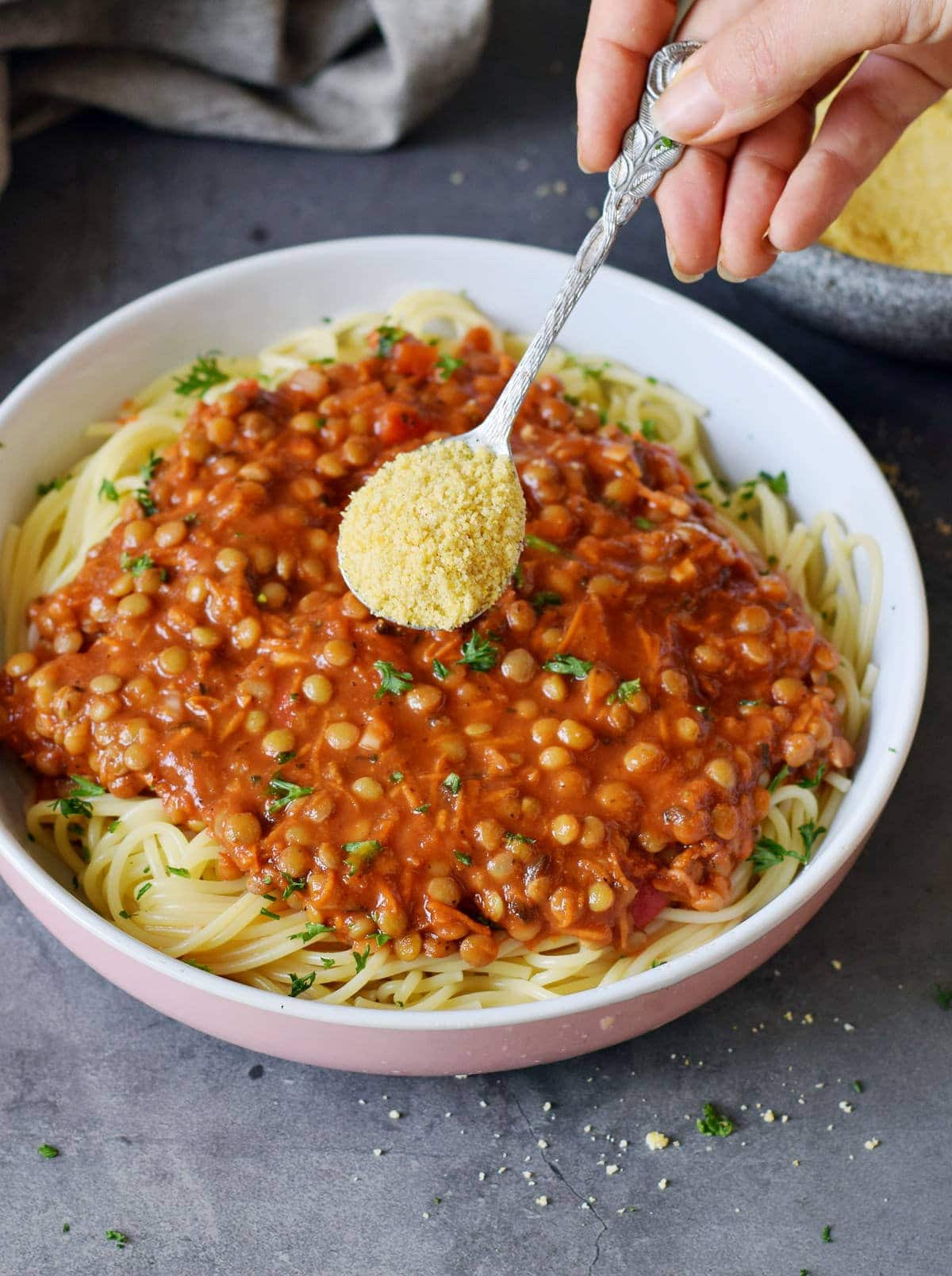 lentil bolognese with hand holding spoon containing parm