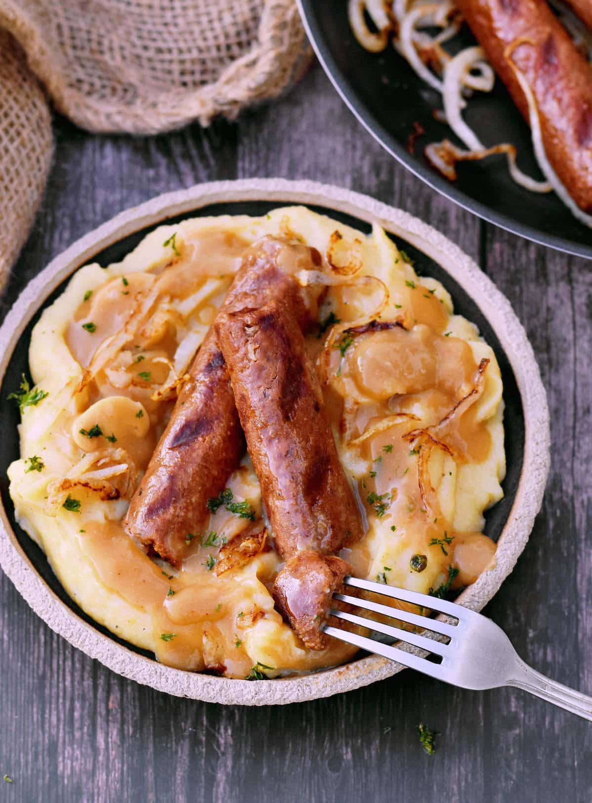 fork submerged in vegan sausage on mashed potatoes