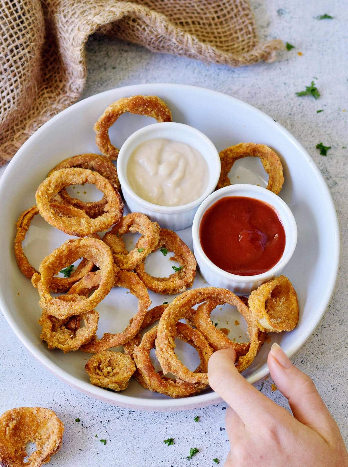 hand grabbing vegan onion rings in a bowl with 2 dips