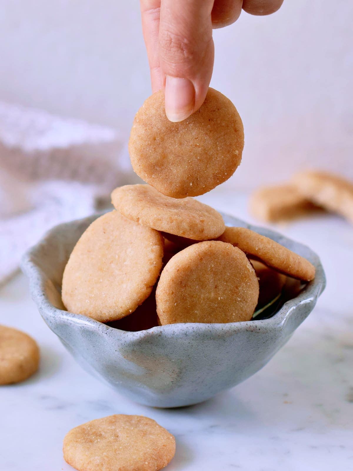 hand hoding one vanilla wafer cookie over ceramic bowl