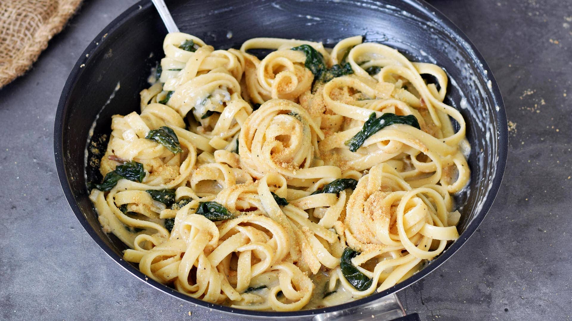 horizontal photo of creamy lemon pasta with spinach in black skillet with fork