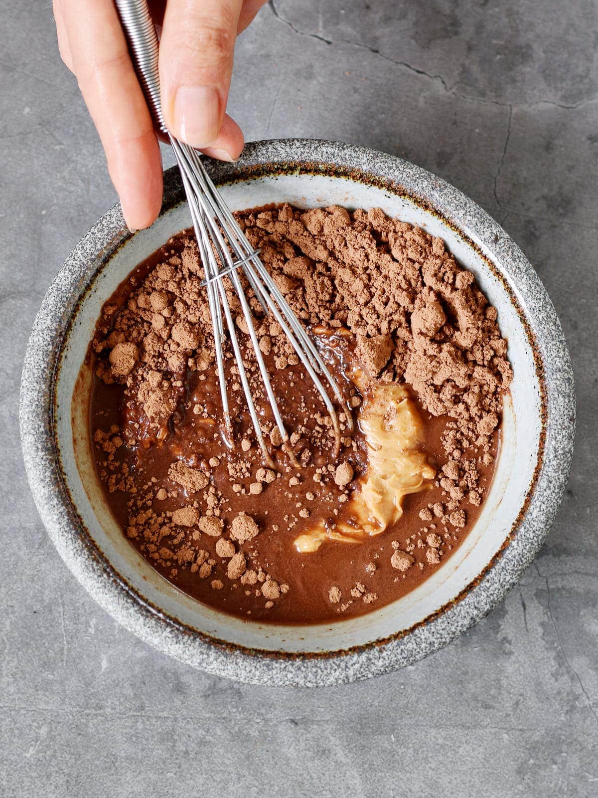 mixing cocoa powder nut butter and maple syrup in a bowl with whisk