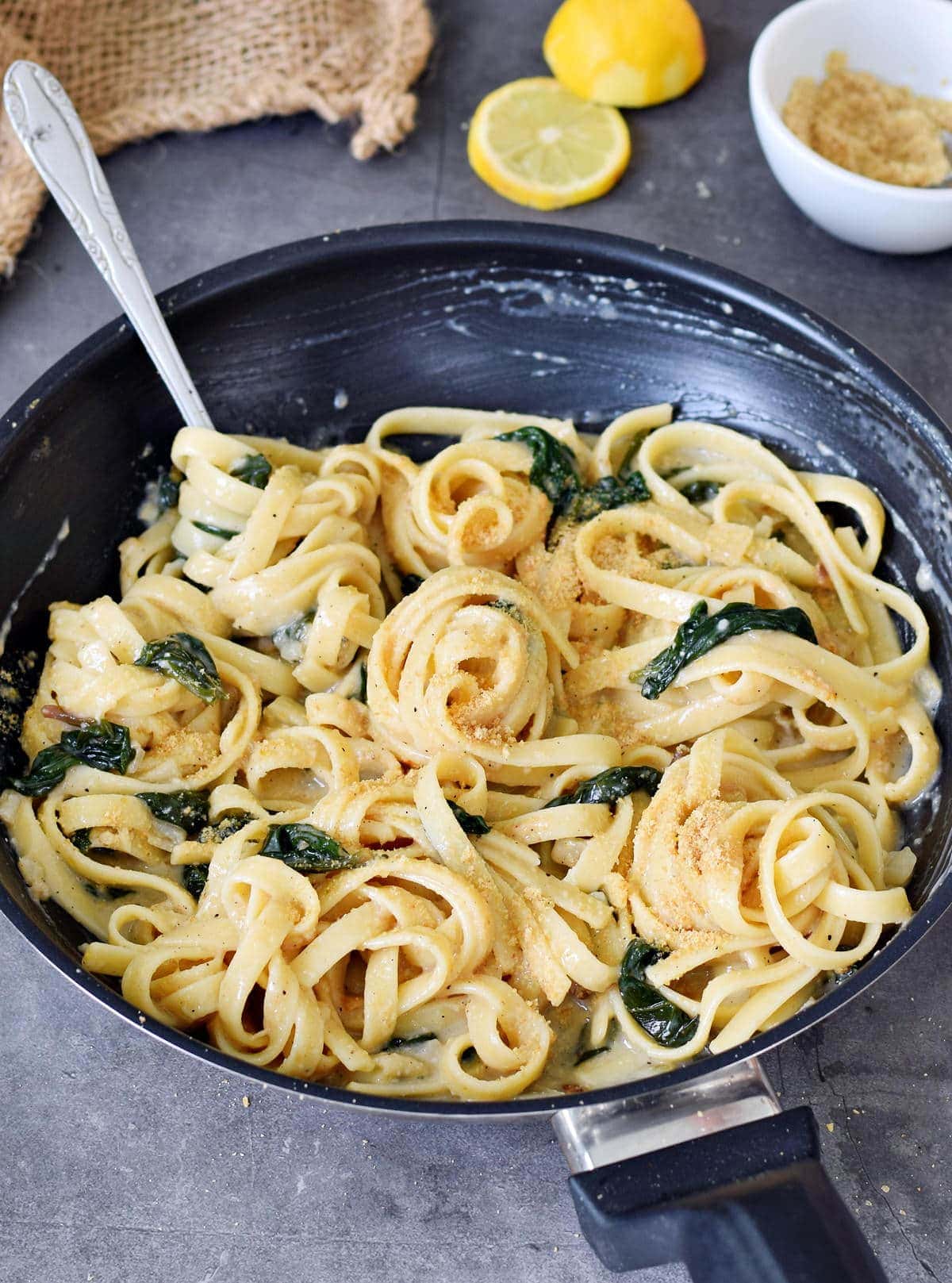 pasta with spinach and lemon cream sauce in black skillet with fork