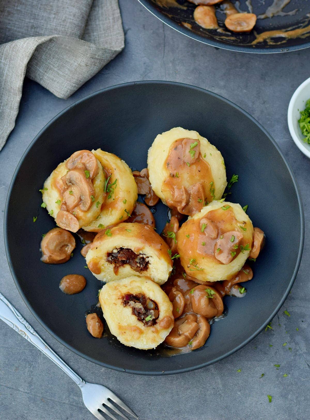 4 Kartoffelklöße, einer mit Champignons gefüllt, mit Bratensoße auf schwarzem Teller