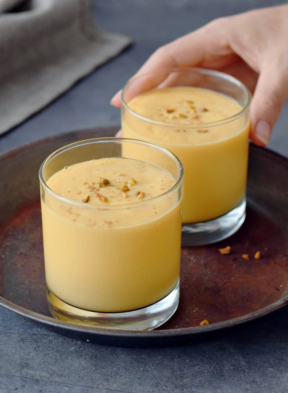 Hand greift nach Glas mit Mango-Smoothie