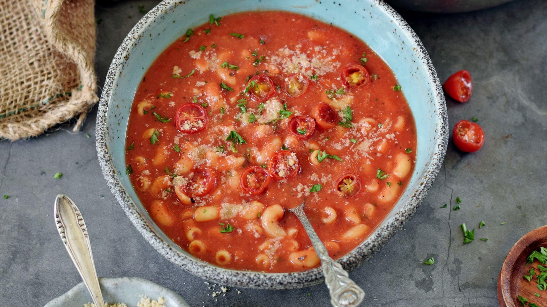 horizontal image of tomato pasta soup in bowl with roasted cherry tomatoes