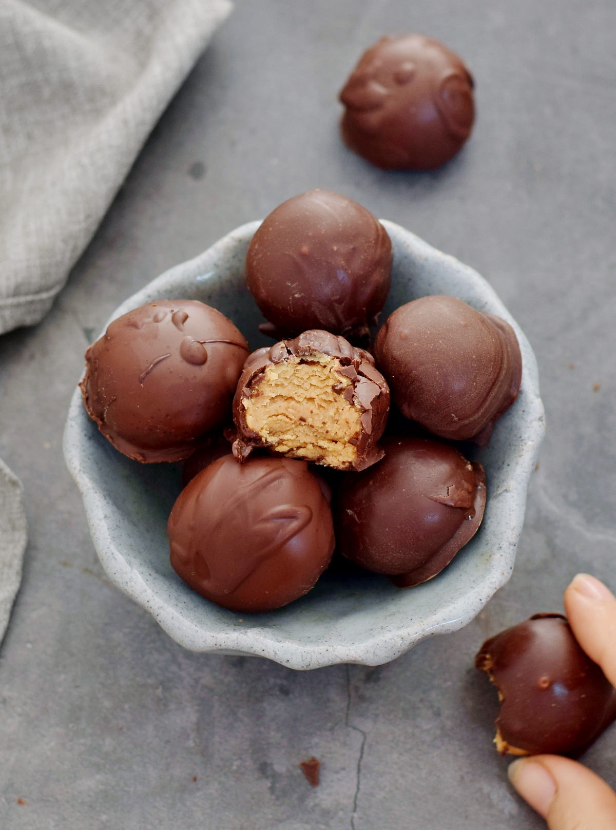 peanut butter balls covered in chocolate in bowl with hand grabbing one