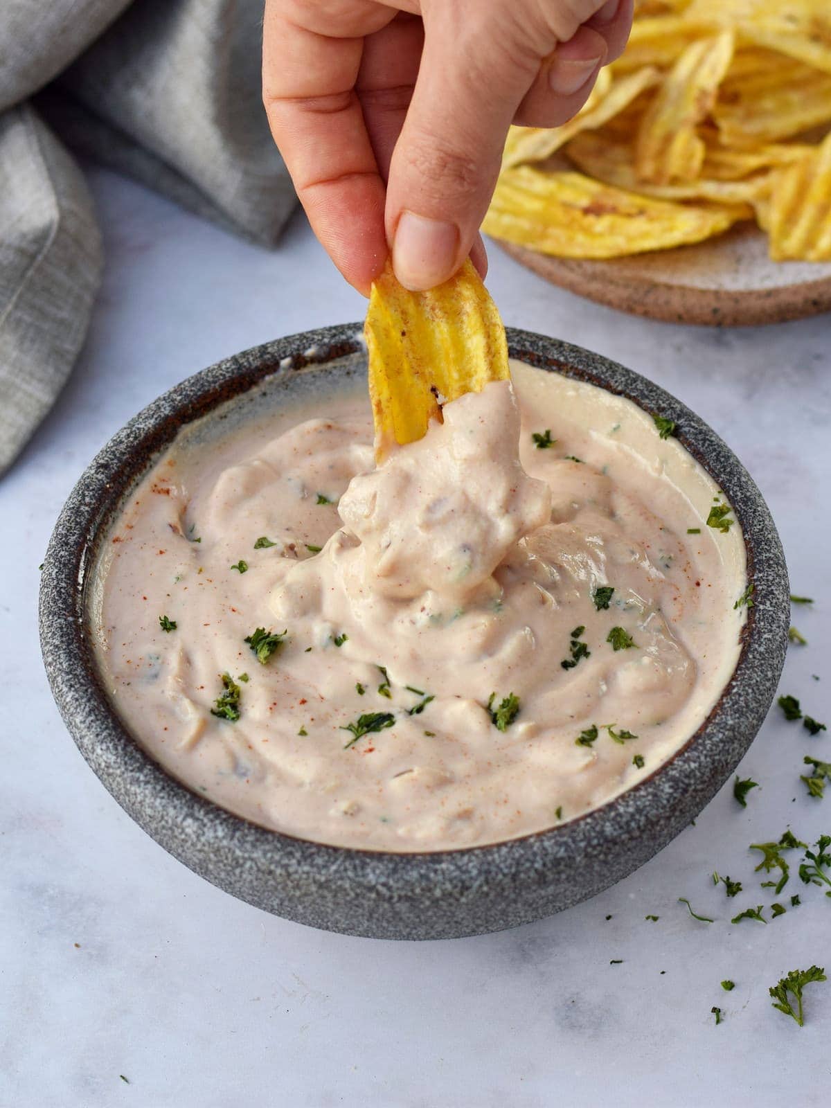 Hand holding chip submerged in vegan French onion dip in bowl