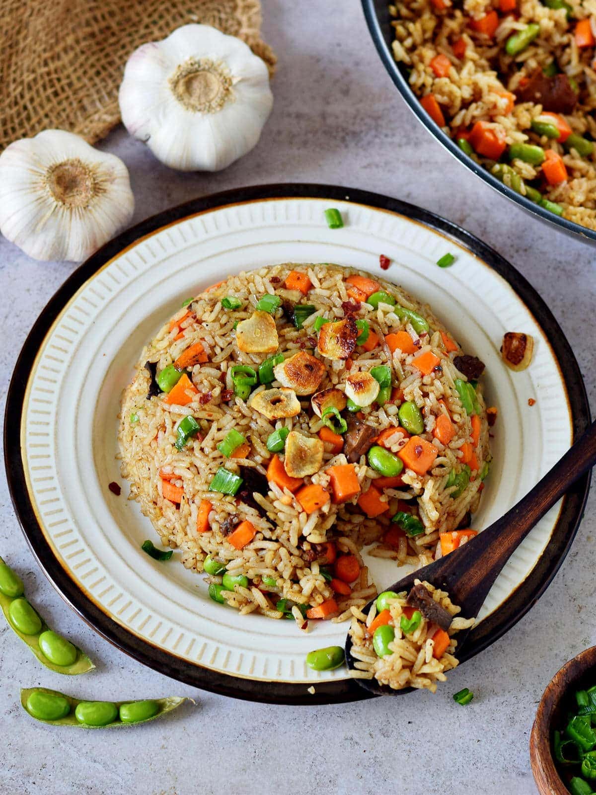 Gebratener Reis mit Gemüse und Knoblauch auf Teller mit Holzlöffel