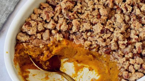 Vegan sweet potato casserole in white round baking pan with spoon