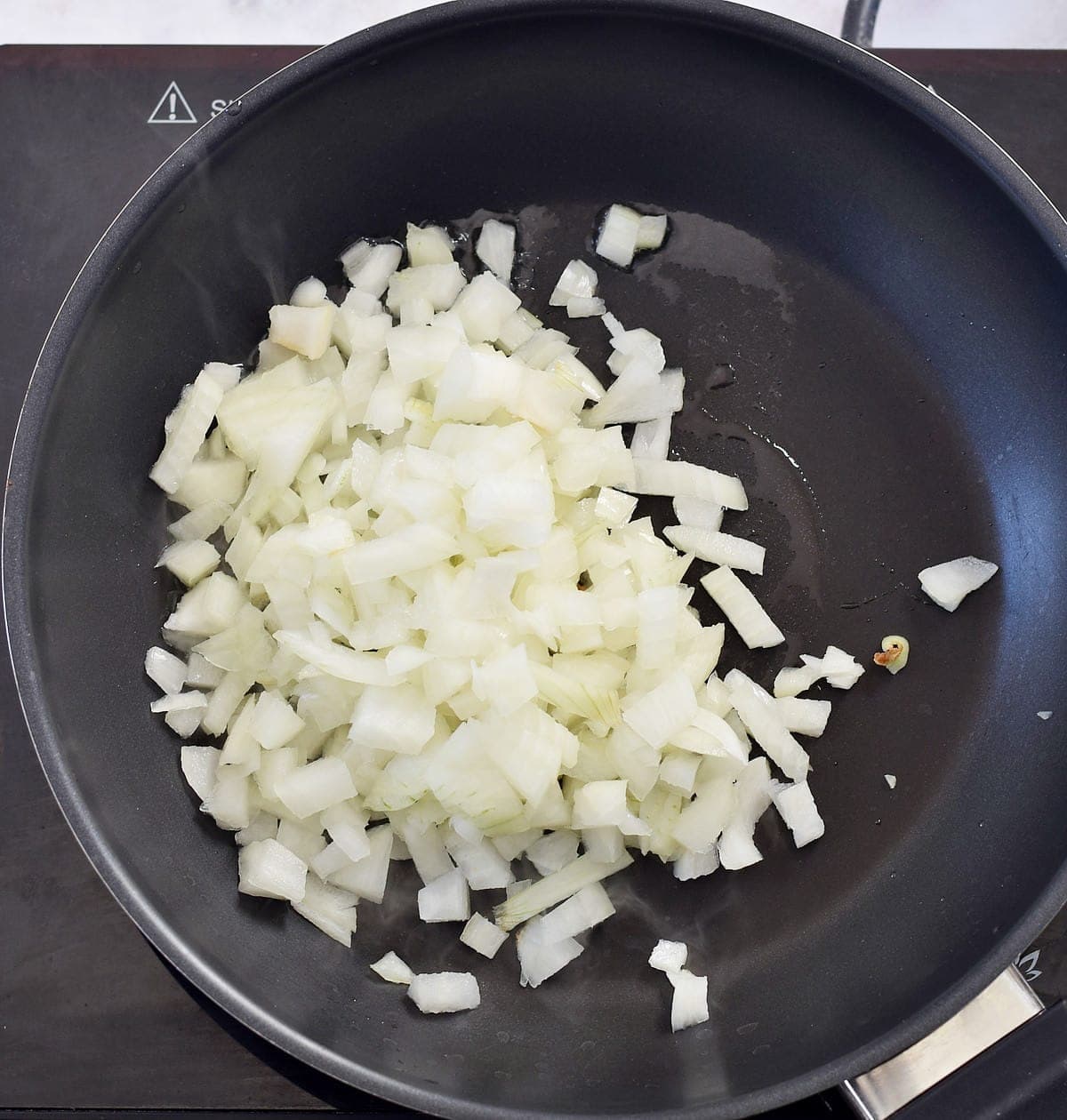 raw diced white onion in black pan