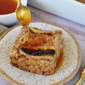 spoon drizzles maple syrup on a vegan baked oatmeal piece with banana on small plate