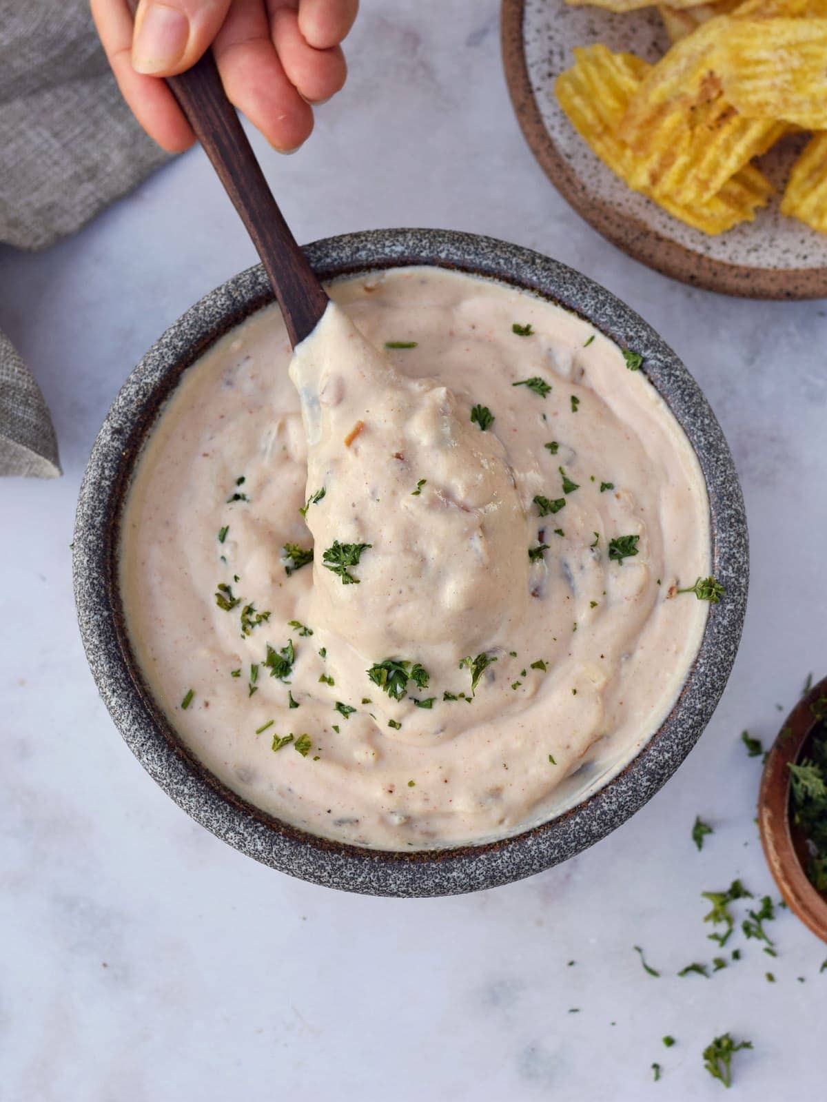 stirring dairy-free sour cream dip with wooden spoon in bowl