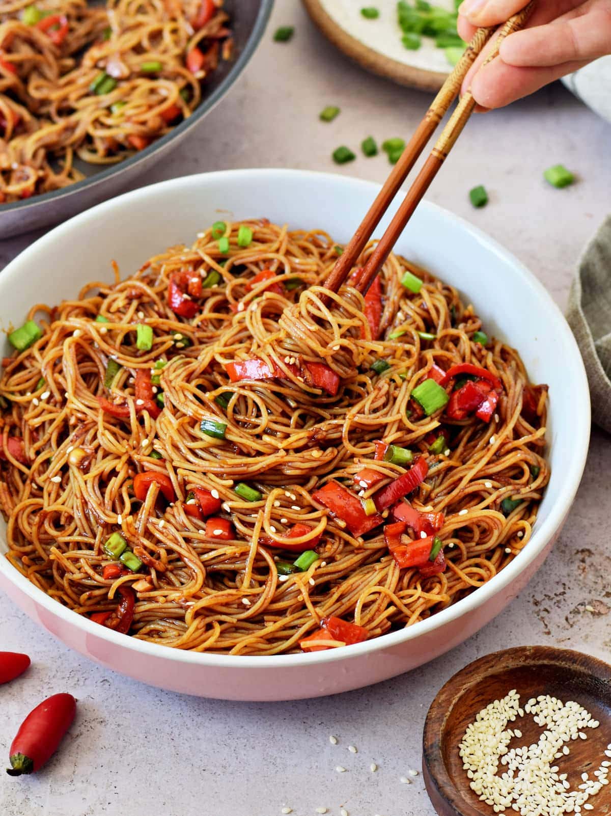 vegan spicy noodles in bowl with hot sauce and chopsticks