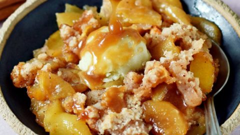 spoon drizzling vegan caramel over apple crisp (without oats) with ice cream on plate