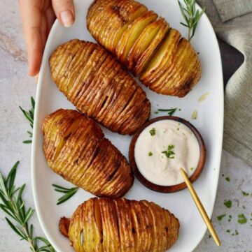 Hand holding a plate with crispy Hasselback potatoes and dip