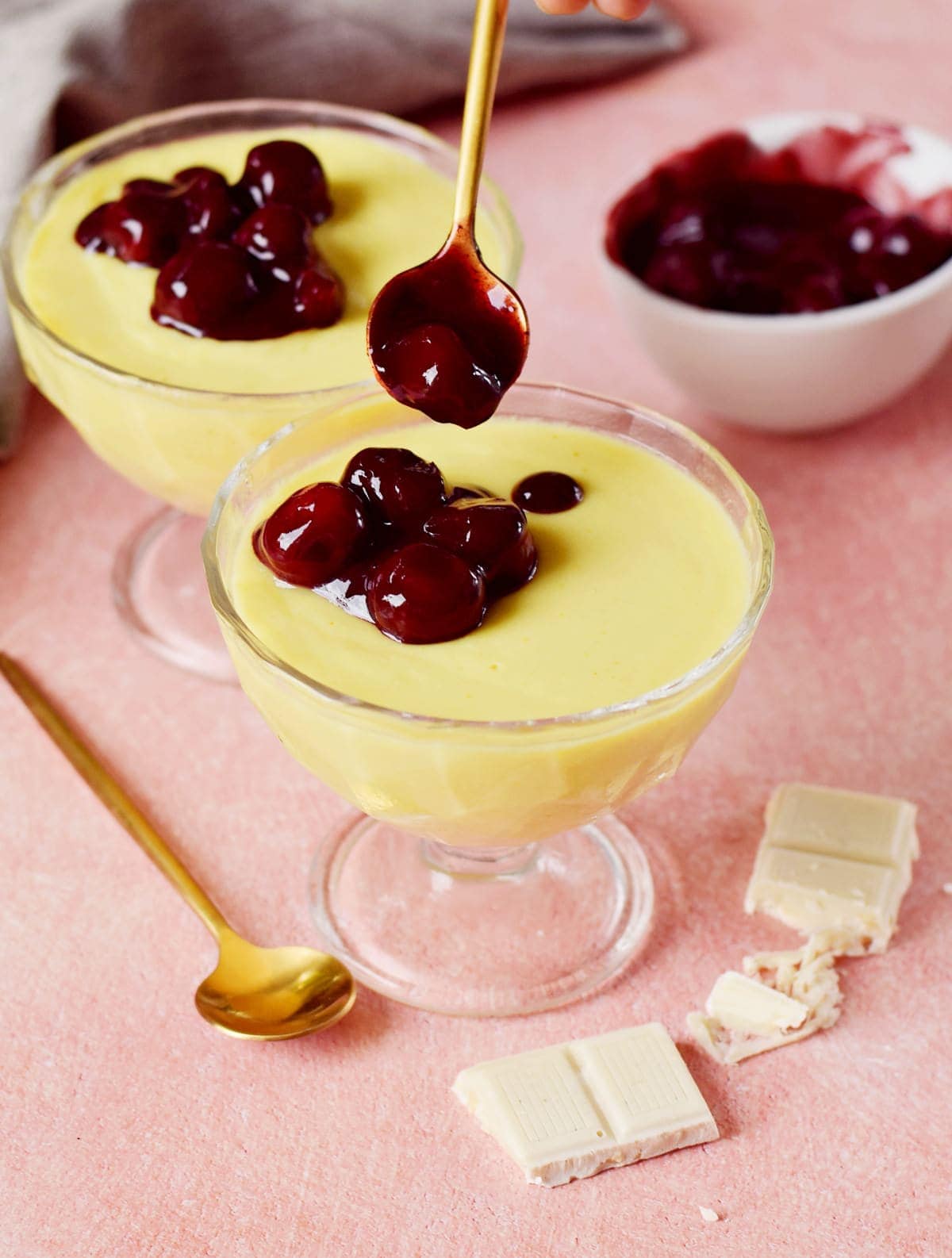 cherry compote being spooned on vegan vanilla pudding in a glass