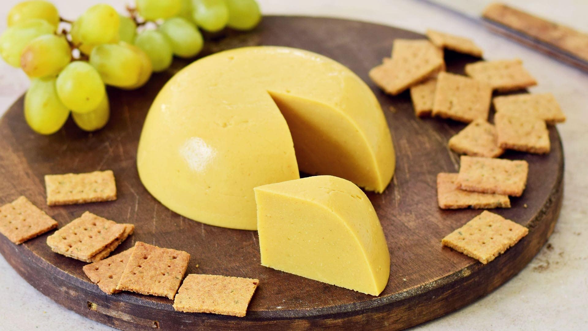 horizontale Aufnahme von Käsesersatz (selbstgemacht) auf Holzbrett mit Crackern und Trauben
