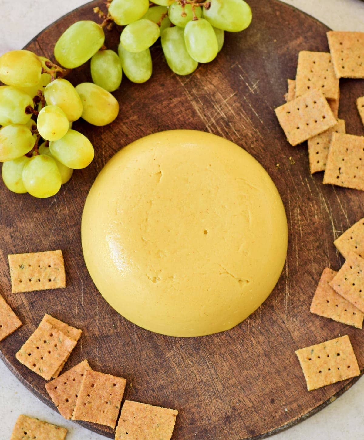 top view of plant-based queso on wooden board with crackers and grapes from above
